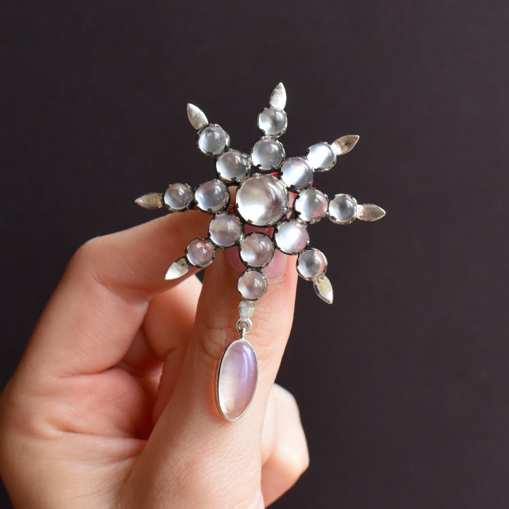 A Victorian silver starburst brooch set with round cabochon moonstones and a suspended oval moonstone drop. View X
