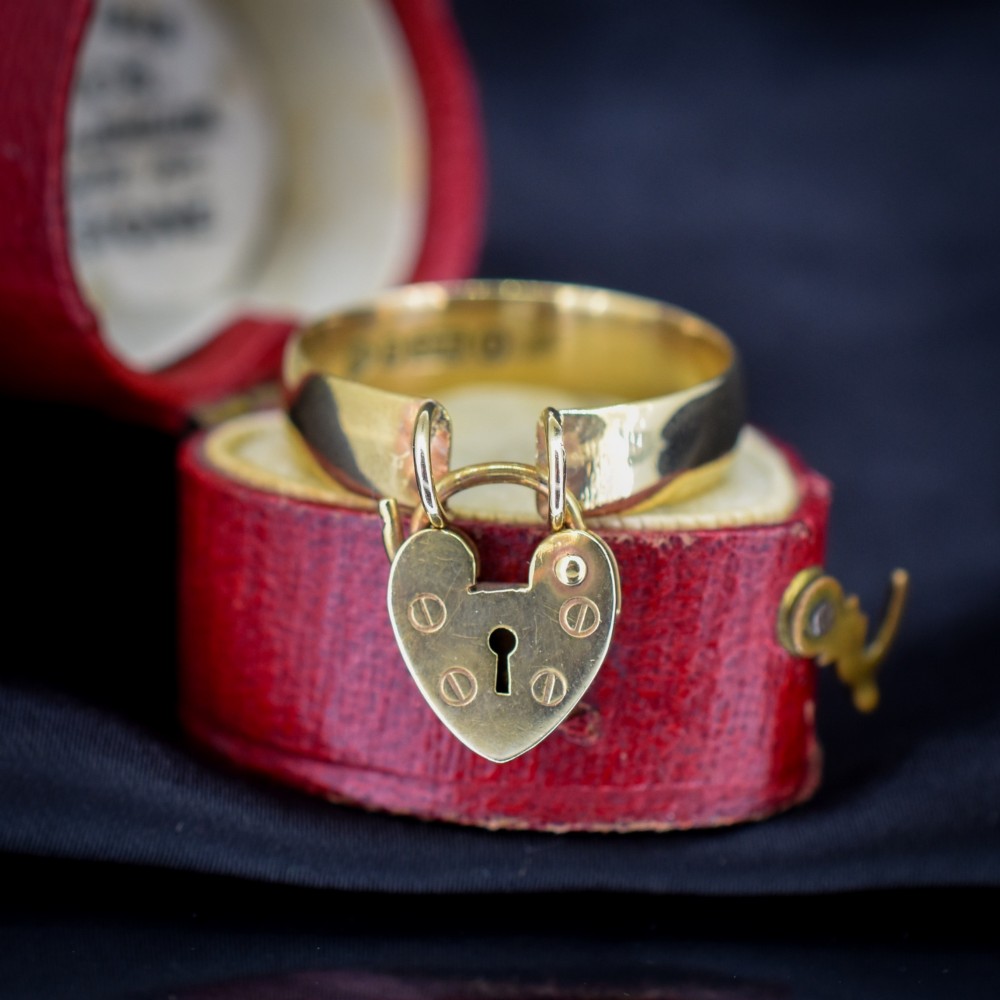 A late Victorian 9ct yellow gold band ring featuring a suspended heart-shaped padlock charm with keyhole detail.