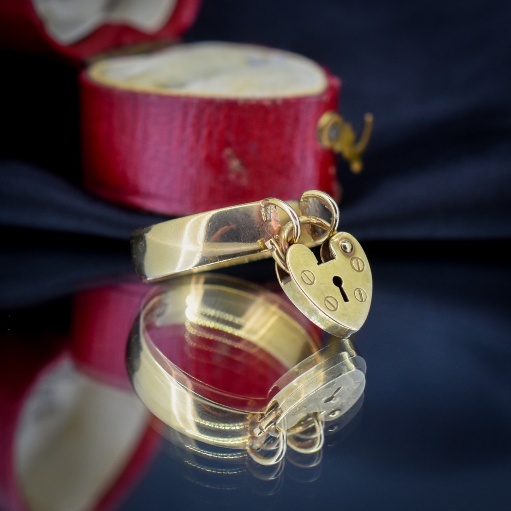A late Victorian 9ct yellow gold band ring featuring a suspended heart-shaped padlock charm with keyhole detail. View IV