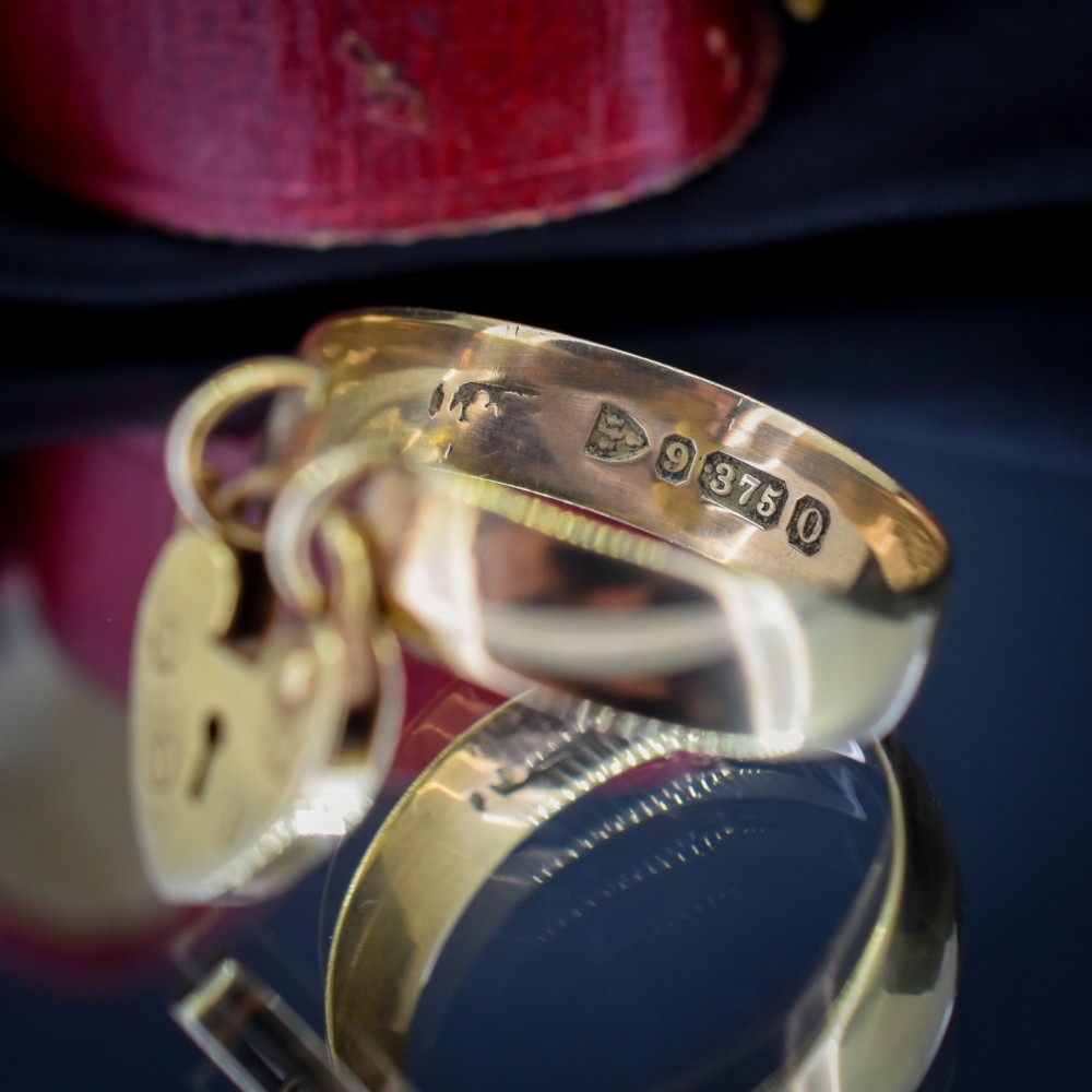 A late Victorian 9ct yellow gold band ring featuring a suspended heart-shaped padlock charm with keyhole detail. View VI