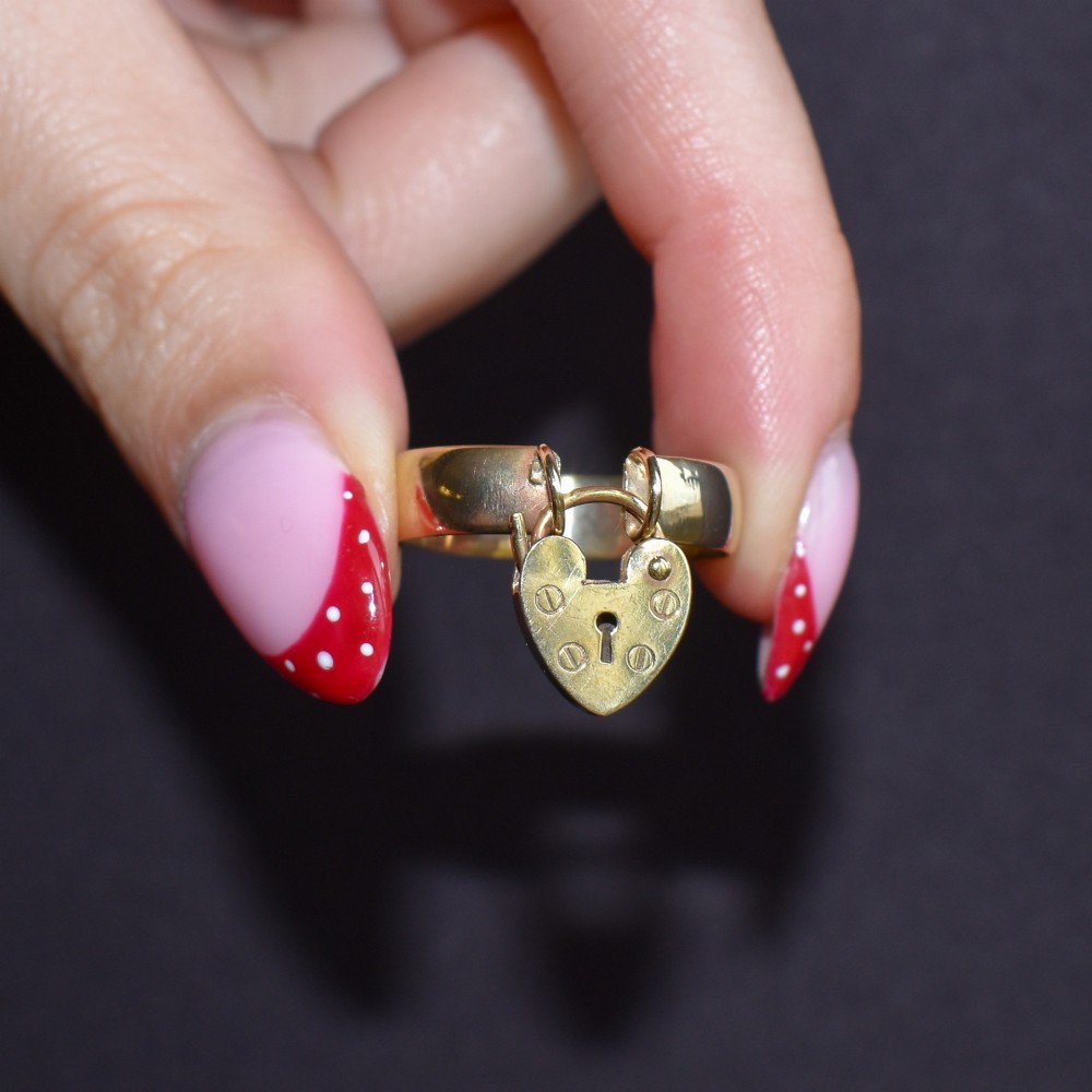A late Victorian 9ct yellow gold band ring featuring a suspended heart-shaped padlock charm with keyhole detail. View VIII