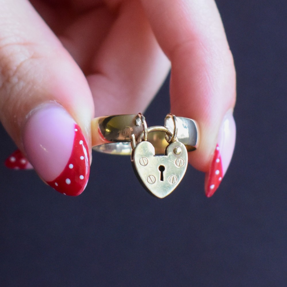 A late Victorian 9ct yellow gold band ring featuring a suspended heart-shaped padlock charm with keyhole detail. View IX