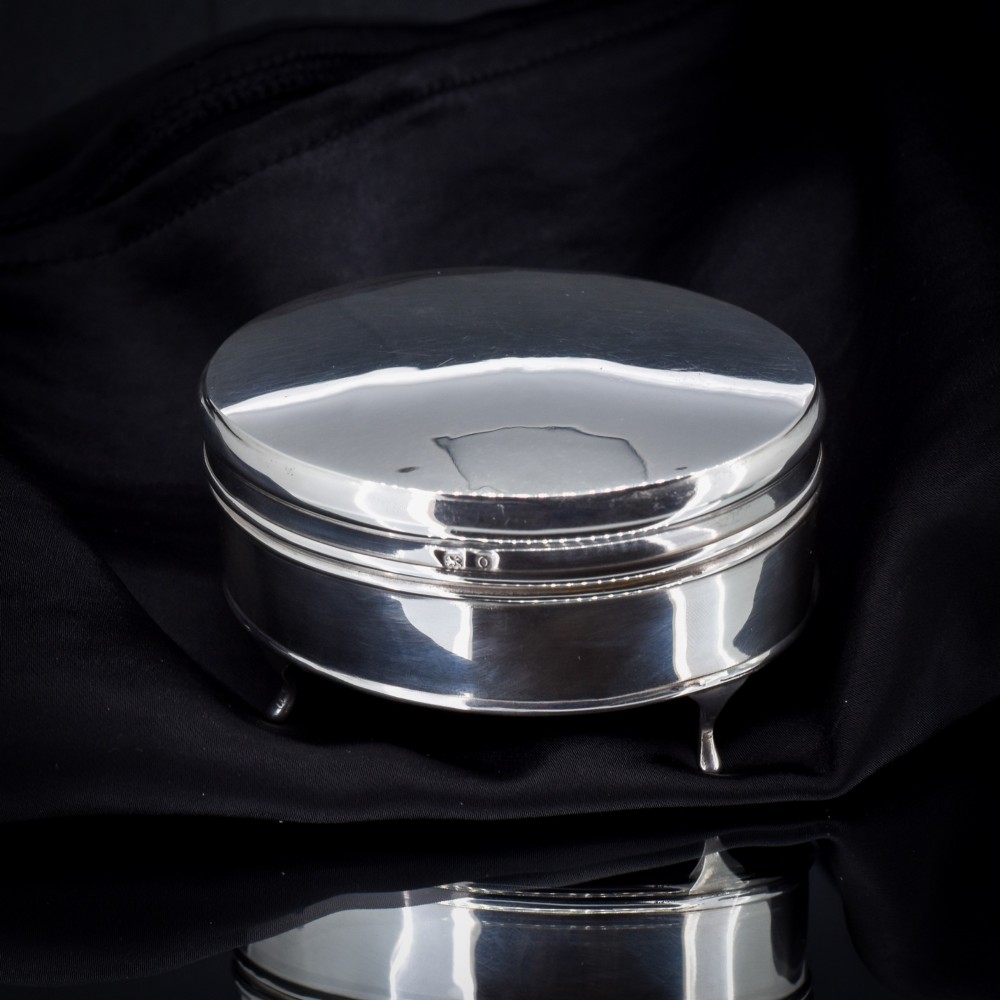 An oval sterling silver trinket box with a smooth polished hinged lid supported on four small cabriole feet.