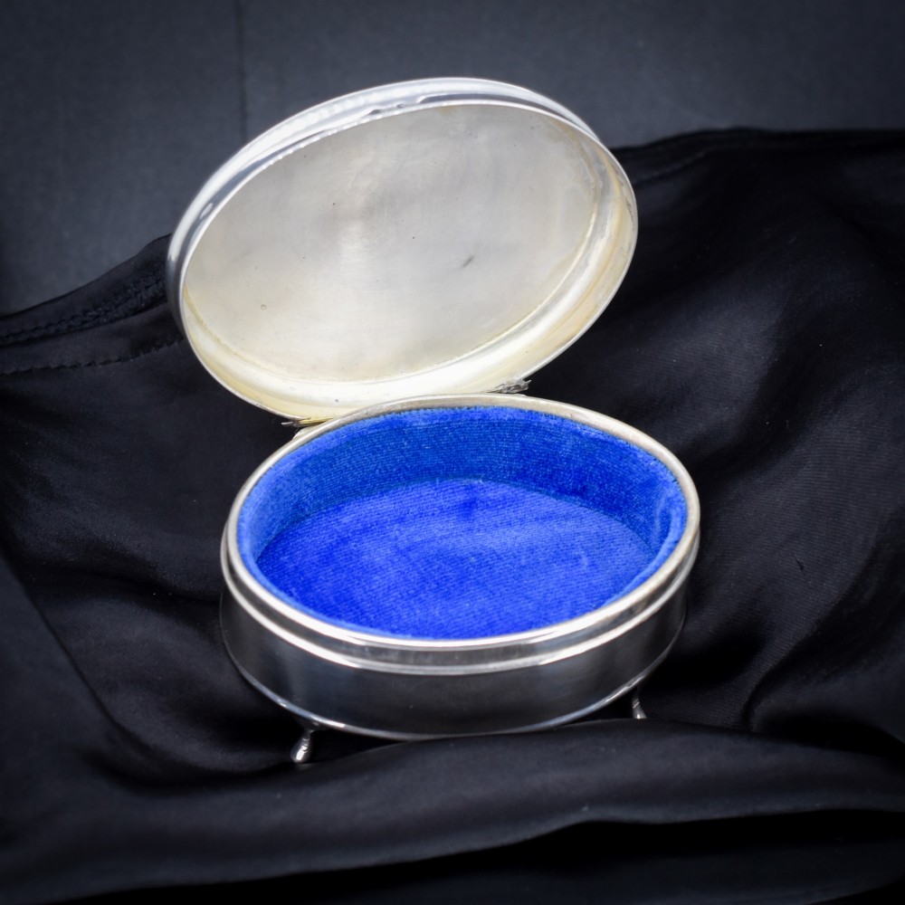 An oval sterling silver trinket box with a smooth polished hinged lid supported on four small cabriole feet. View V