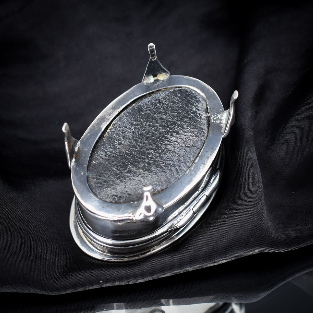 An oval silver trinket box resting on three cabriole legs with a patterned rim along the lid. View III