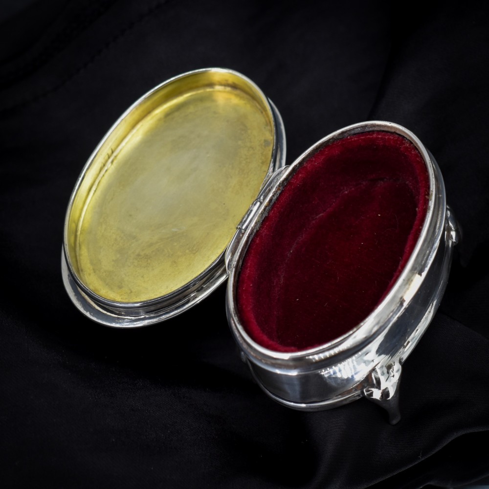 An oval silver trinket box resting on three cabriole legs with a patterned rim along the lid. View IV