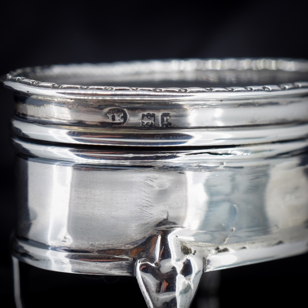 An oval silver trinket box resting on three cabriole legs with a patterned rim along the lid. View VI