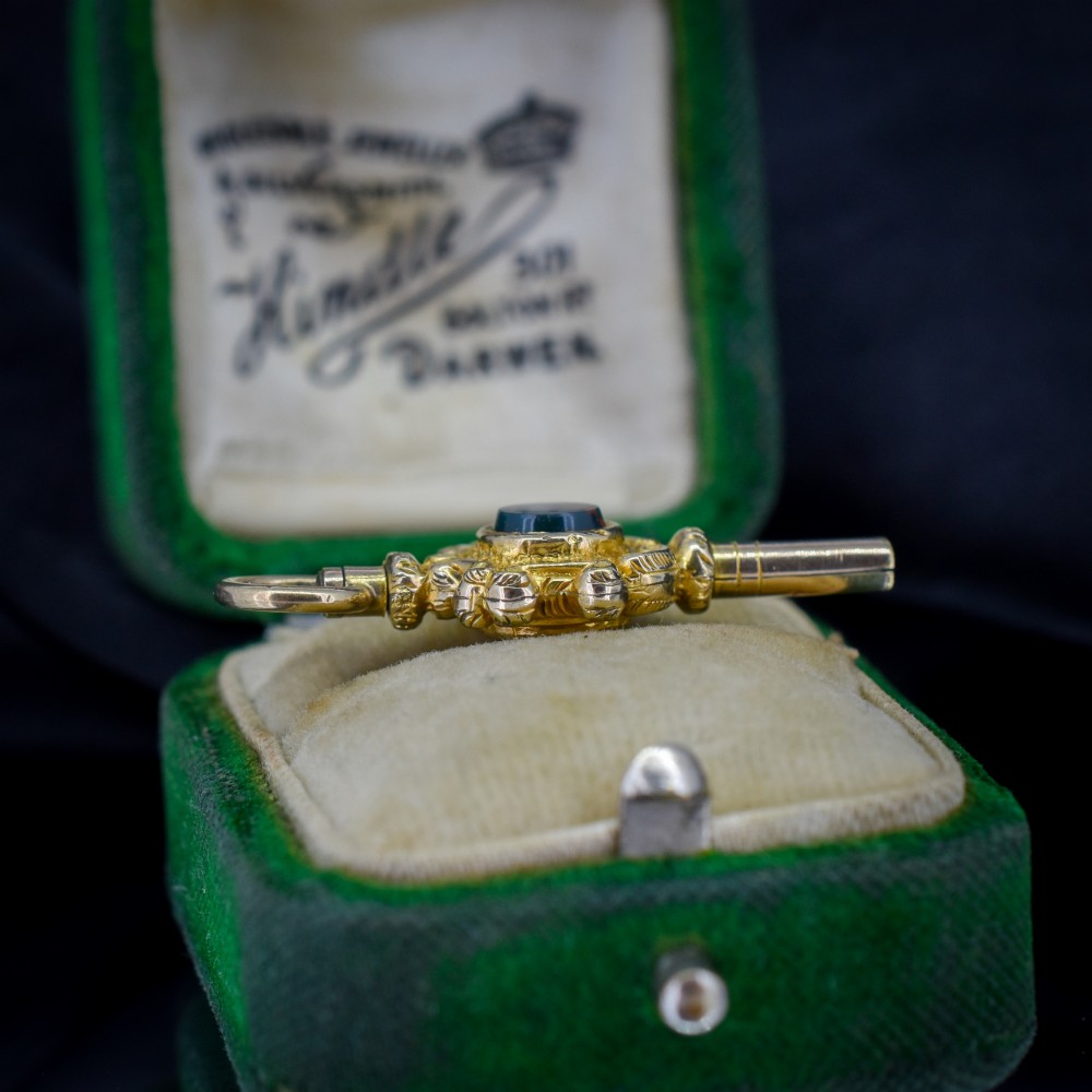 An antique gold watch key pendant featuring scrollwork ornamentation around a central dark green bloodstone seal, topped with a suspension ring. View V