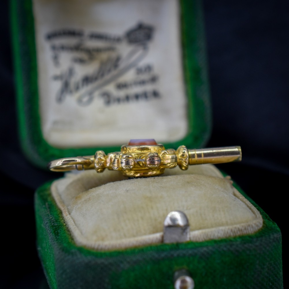 An antique gold watch key pendant featuring scrollwork ornamentation around a central dark green bloodstone seal, topped with a suspension ring. View VI