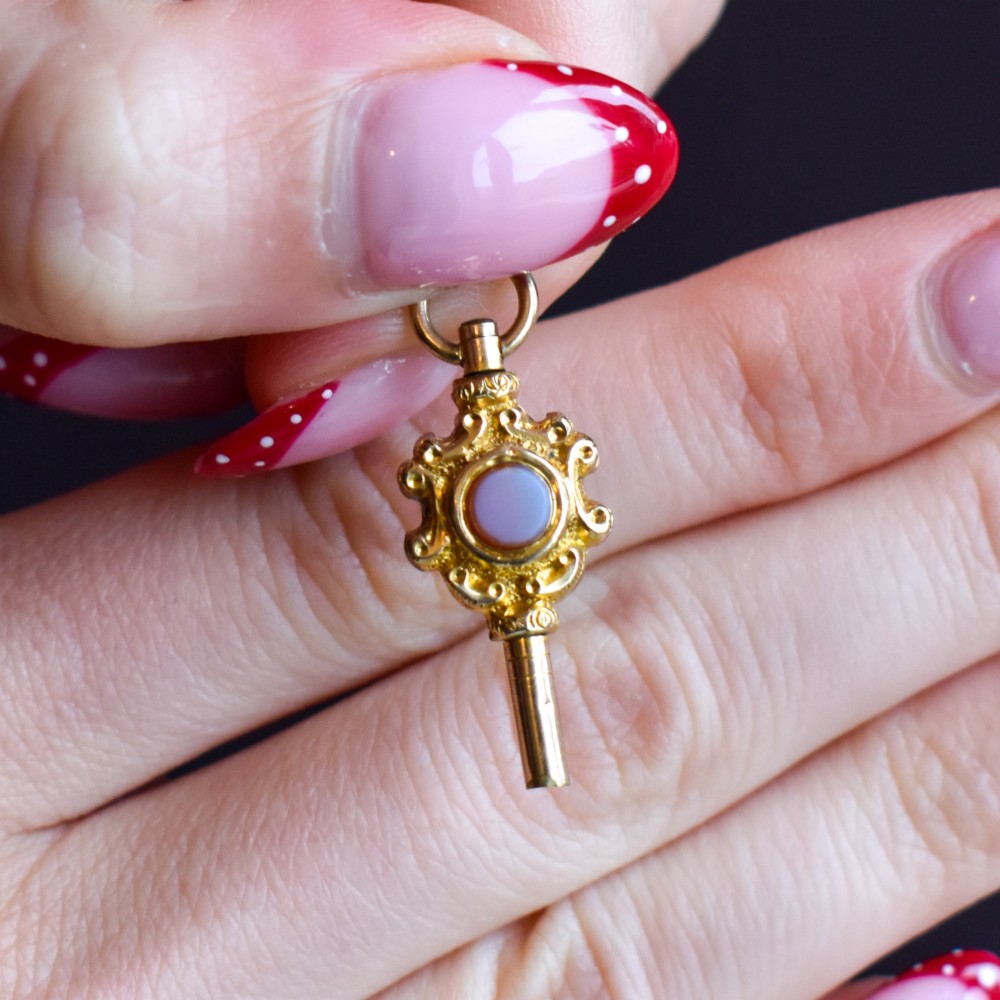 An antique gold watch key pendant featuring scrollwork ornamentation around a central dark green bloodstone seal, topped with a suspension ring. View VIII