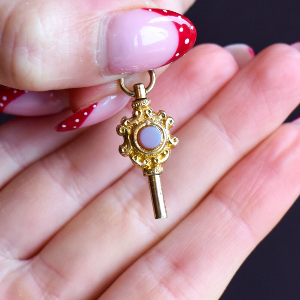An antique gold watch key pendant featuring scrollwork ornamentation around a central dark green bloodstone seal, topped with a suspension ring. View IX
