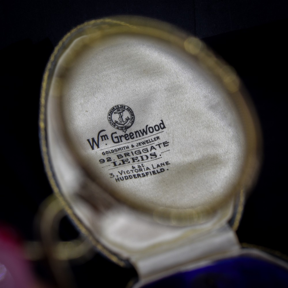 A Georgian rolled gold quizzing glass pendant featuring an engraved circular bezel and an S-scroll handle, resting inside a velvet-lined case. View III
