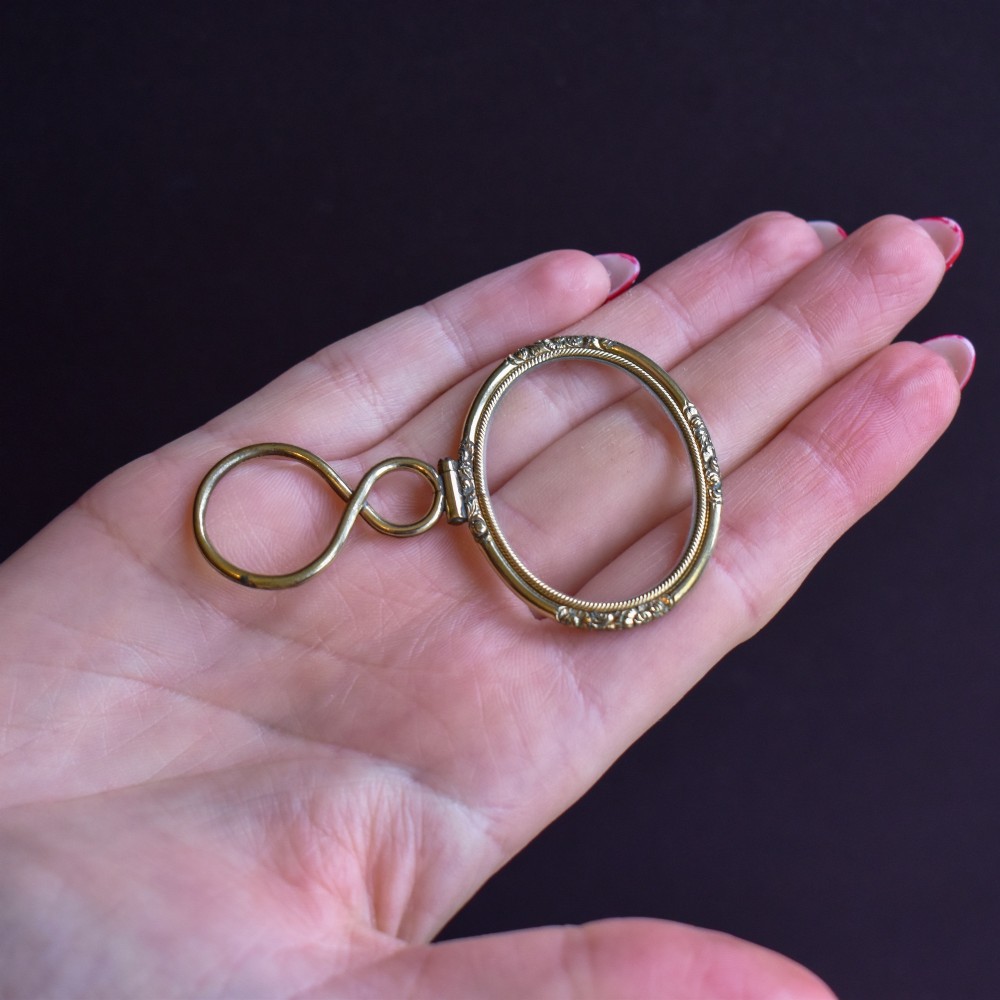 A Georgian rolled gold quizzing glass pendant featuring an engraved circular bezel and an S-scroll handle, resting inside a velvet-lined case. View VII