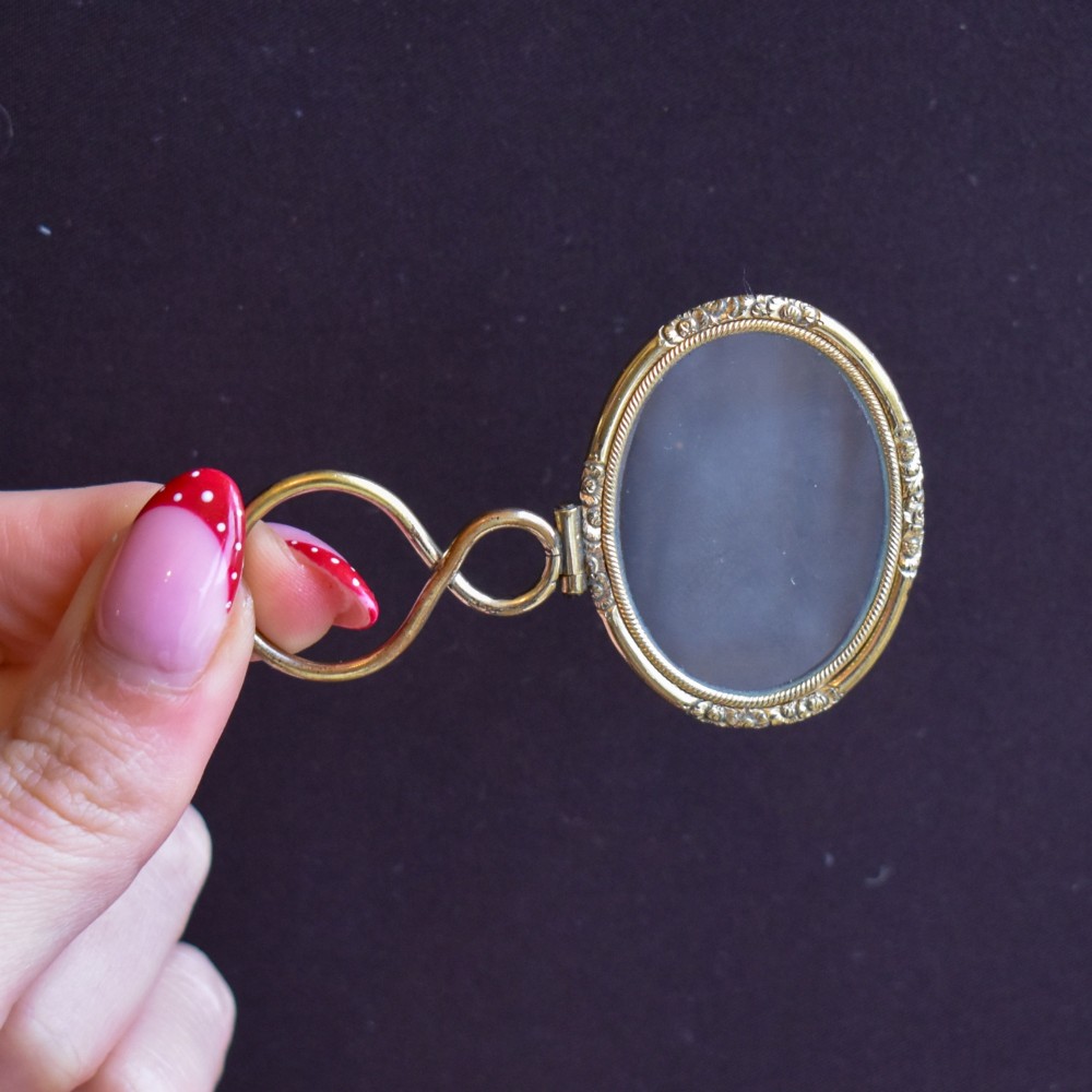 A Georgian rolled gold quizzing glass pendant featuring an engraved circular bezel and an S-scroll handle, resting inside a velvet-lined case. View VIII