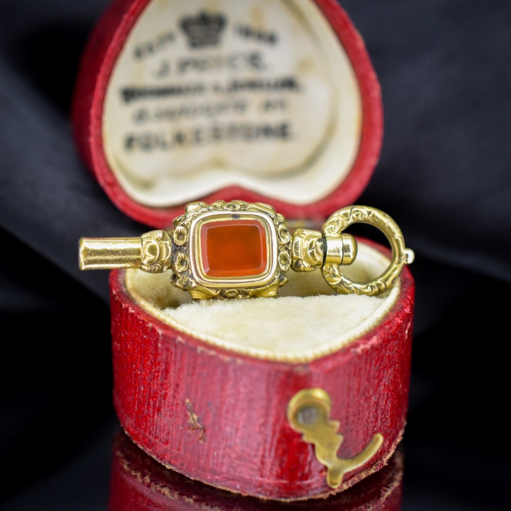 An antique gold-cased pocket watch key pendant inset with a square red agate stone and decorated with intricate chased patterns.
