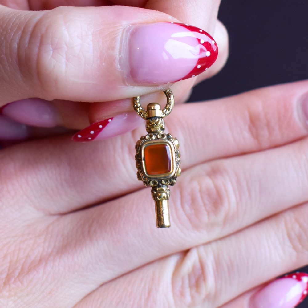 An antique gold-cased pocket watch key pendant inset with a square red agate stone and decorated with intricate chased patterns. View VI
