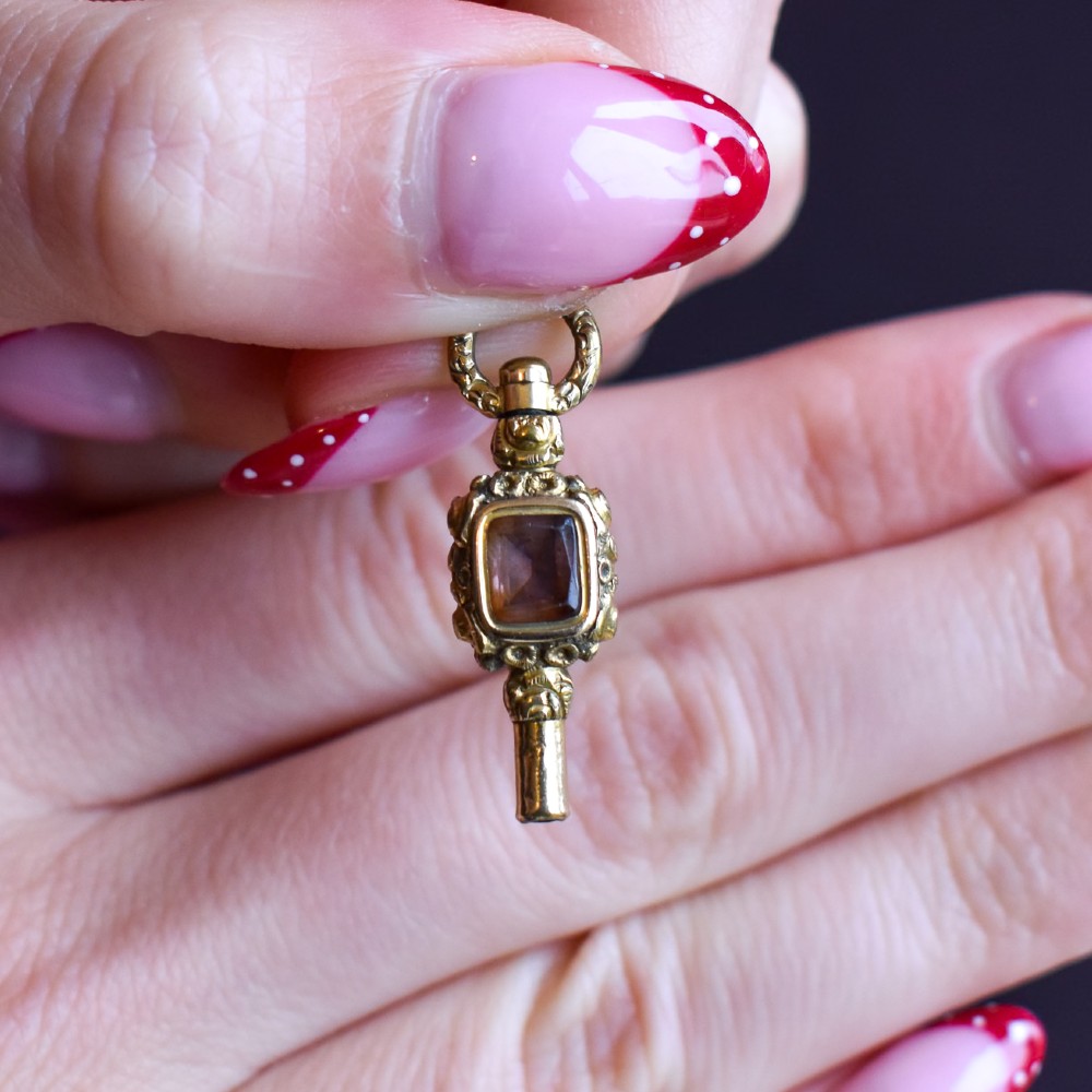 An antique gold-cased pocket watch key pendant inset with a square red agate stone and decorated with intricate chased patterns. View VII