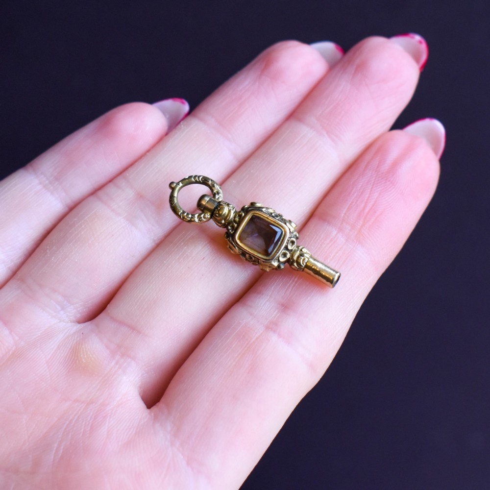 An antique gold-cased pocket watch key pendant inset with a square red agate stone and decorated with intricate chased patterns. View VIII