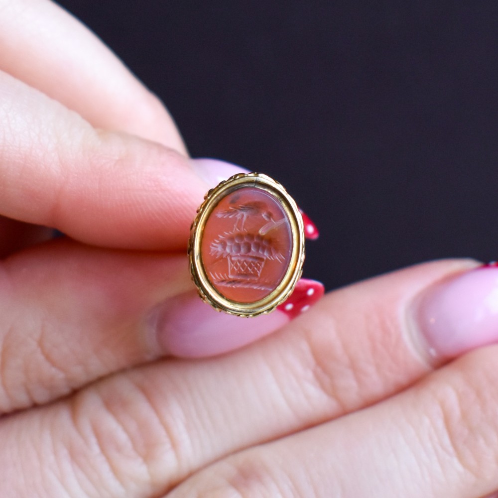 An oval orange-red carnelian gem carved with an intaglio mother bird motif, set within a chased gold-cased fob mount. View IX