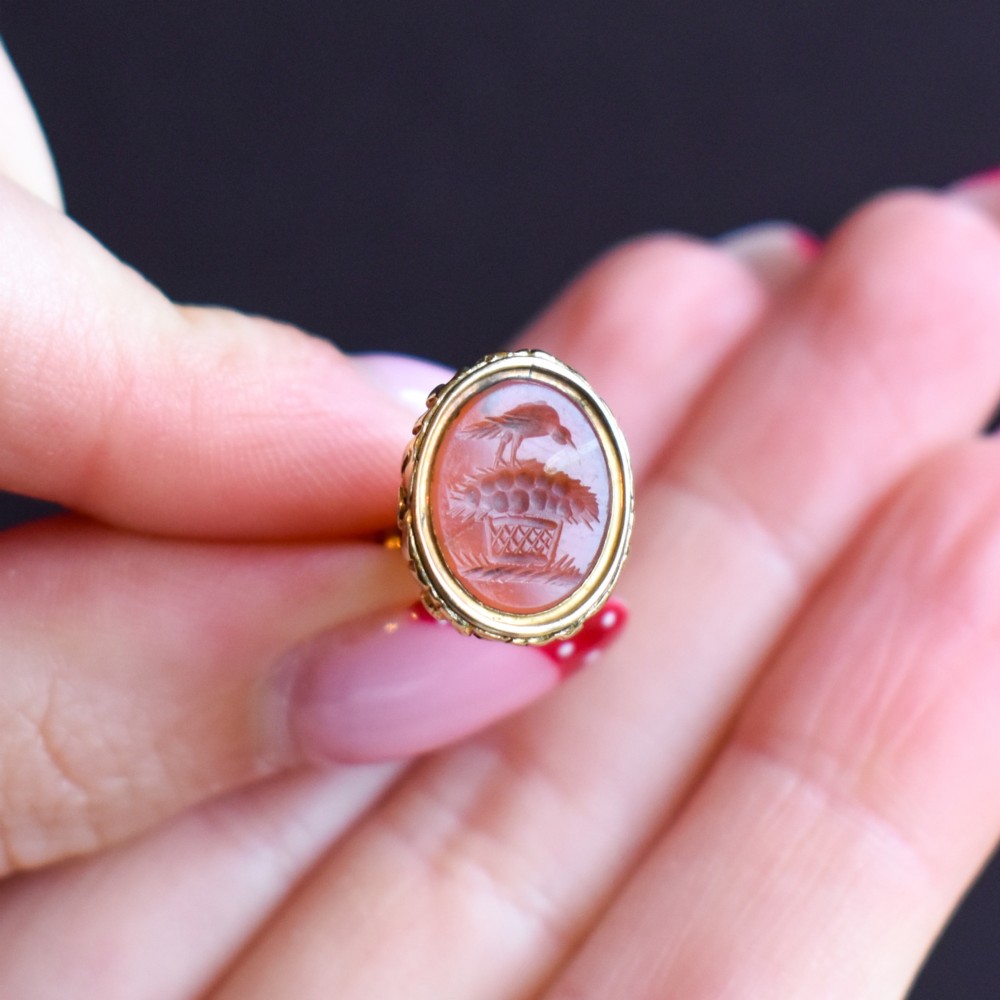 An oval orange-red carnelian gem carved with an intaglio mother bird motif, set within a chased gold-cased fob mount. View X