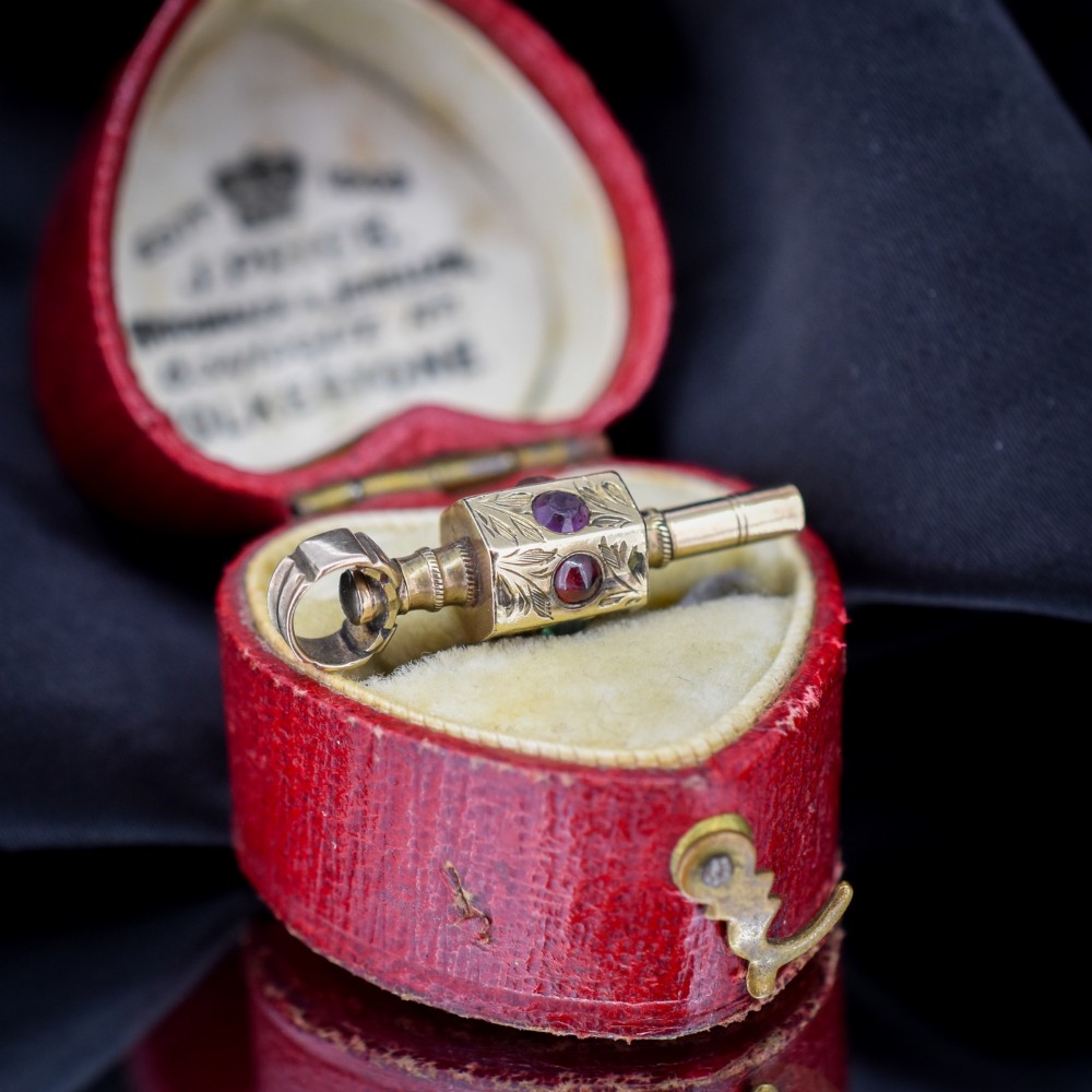 An antique yellow gold barrel watch key fob pendant with engraved scrollwork and a vertical setting of acrostic gemstones. View II