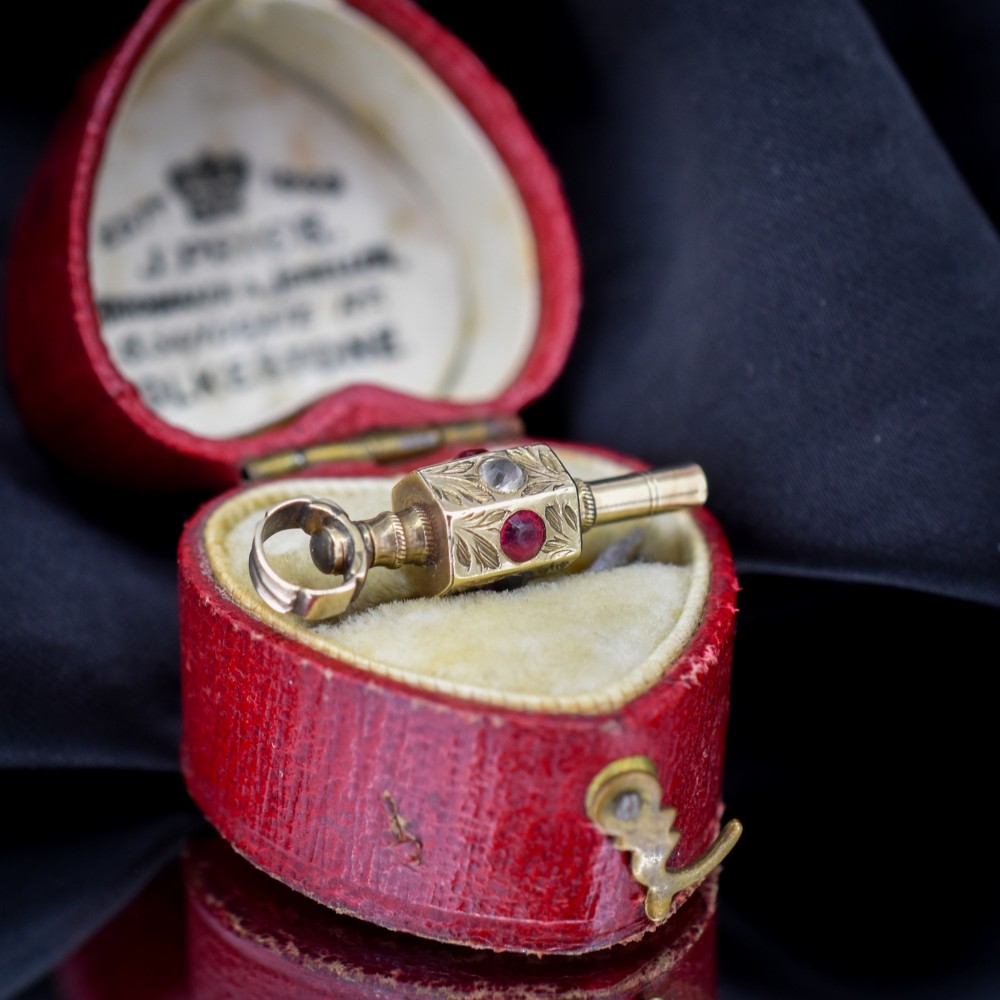 An antique yellow gold barrel watch key fob pendant with engraved scrollwork and a vertical setting of acrostic gemstones. View III