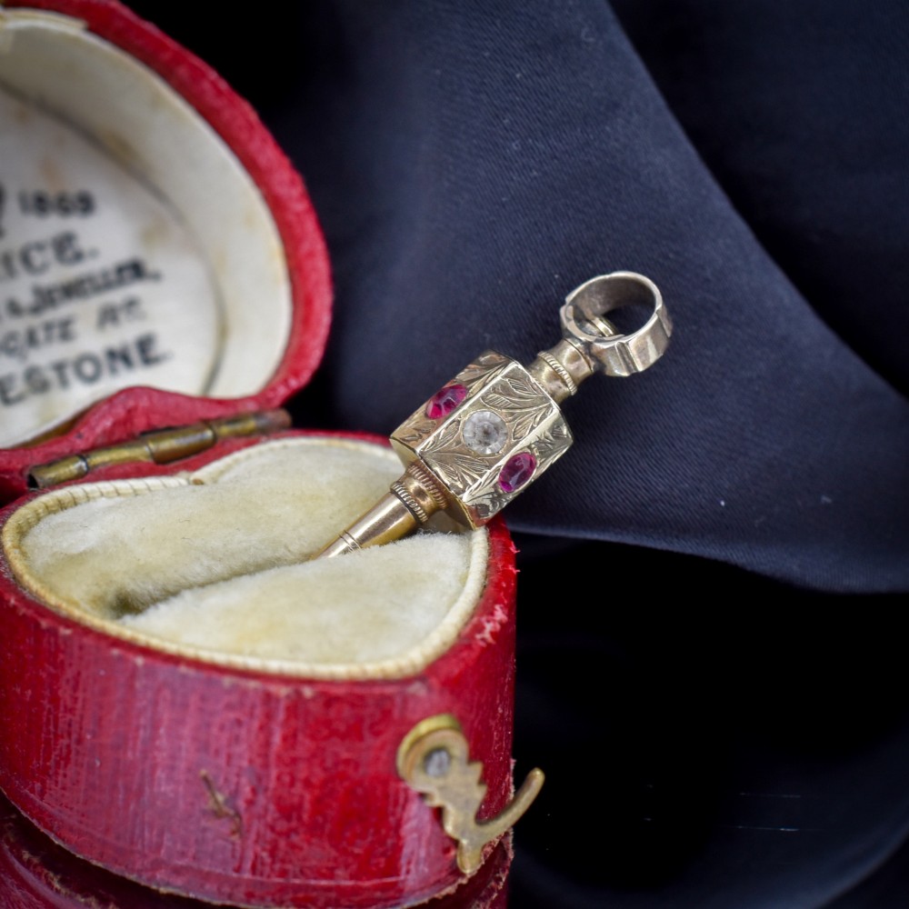 An antique yellow gold barrel watch key fob pendant with engraved scrollwork and a vertical setting of acrostic gemstones. View IV