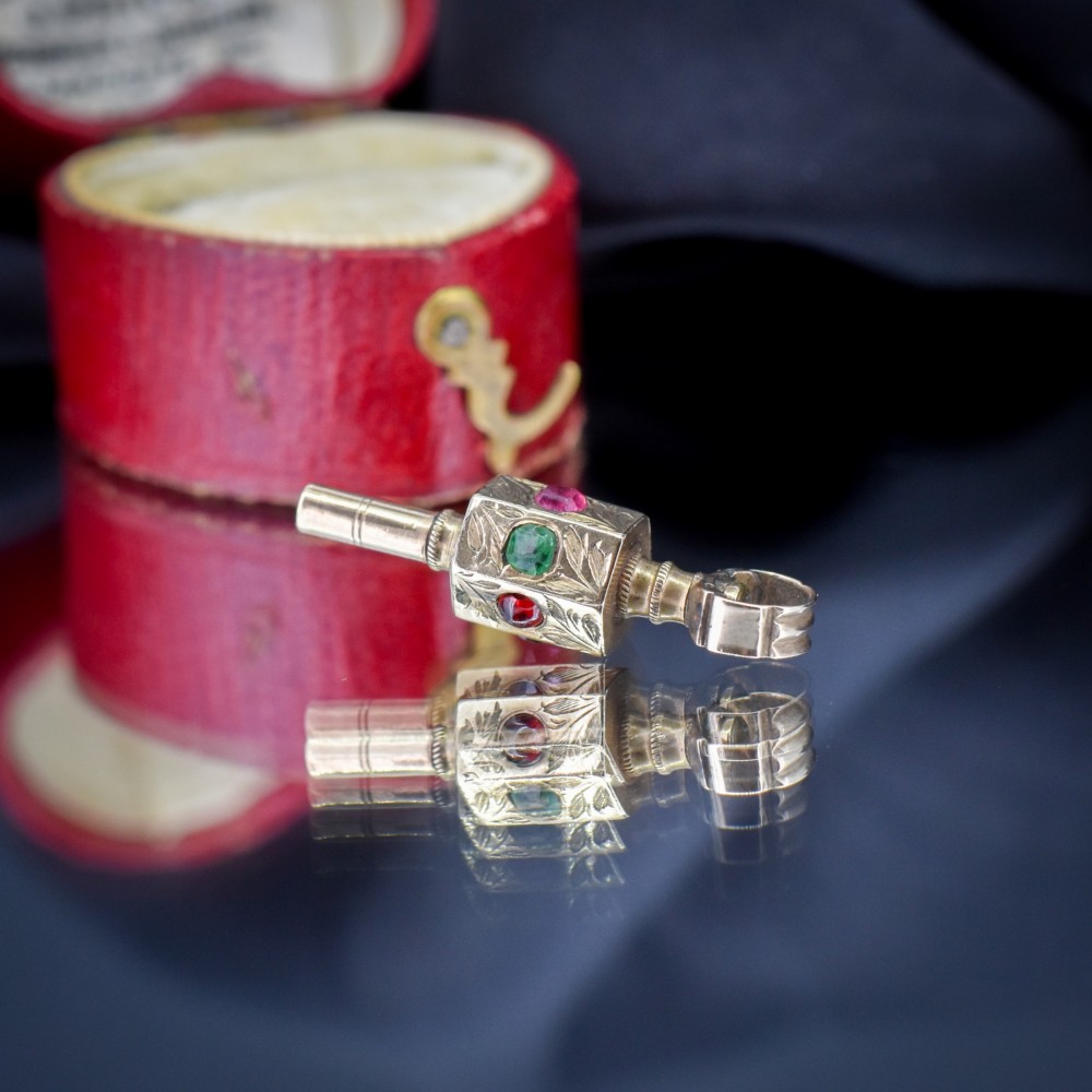 An antique yellow gold barrel watch key fob pendant with engraved scrollwork and a vertical setting of acrostic gemstones. View VI