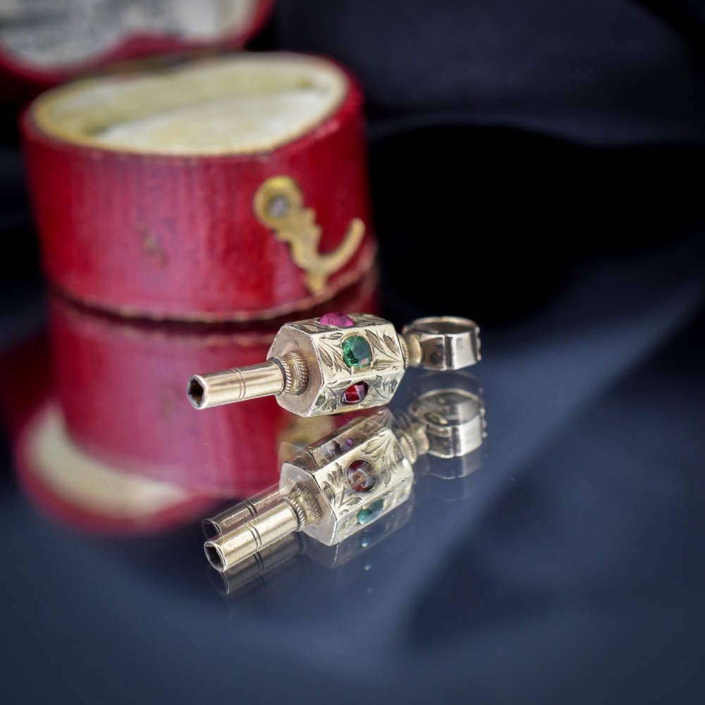 An antique yellow gold barrel watch key fob pendant with engraved scrollwork and a vertical setting of acrostic gemstones. View VII