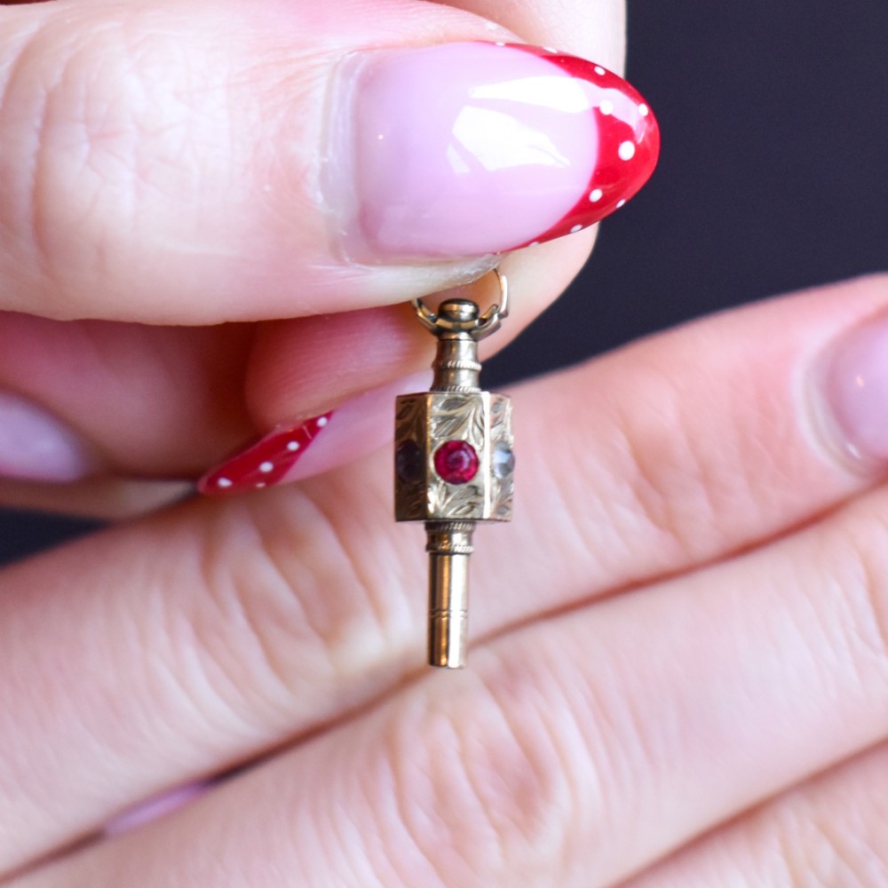An antique yellow gold barrel watch key fob pendant with engraved scrollwork and a vertical setting of acrostic gemstones. View IX