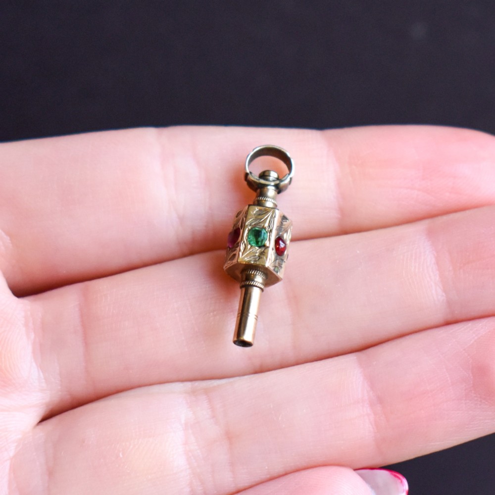 An antique yellow gold barrel watch key fob pendant with engraved scrollwork and a vertical setting of acrostic gemstones. View X
