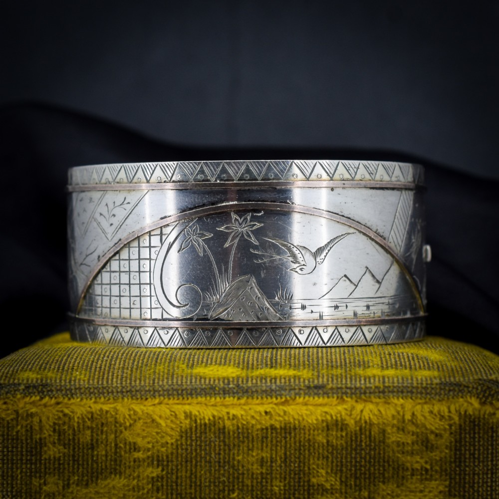 A wide antique silver cuff bangle featuring detailed hand-engraved scenes of a bird in flight, foliage, and geometric borders.