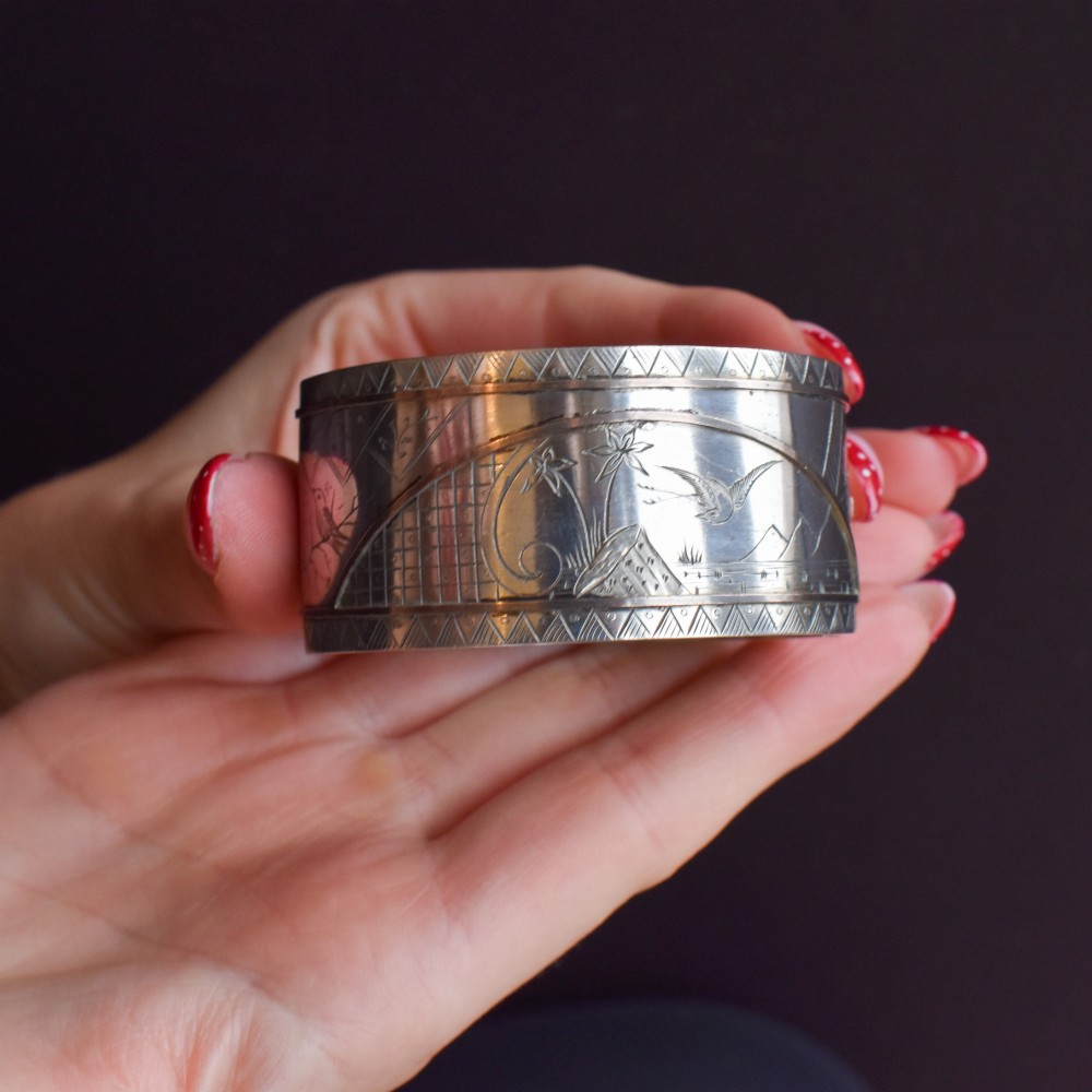 A wide antique silver cuff bangle featuring detailed hand-engraved scenes of a bird in flight, foliage, and geometric borders. View VII