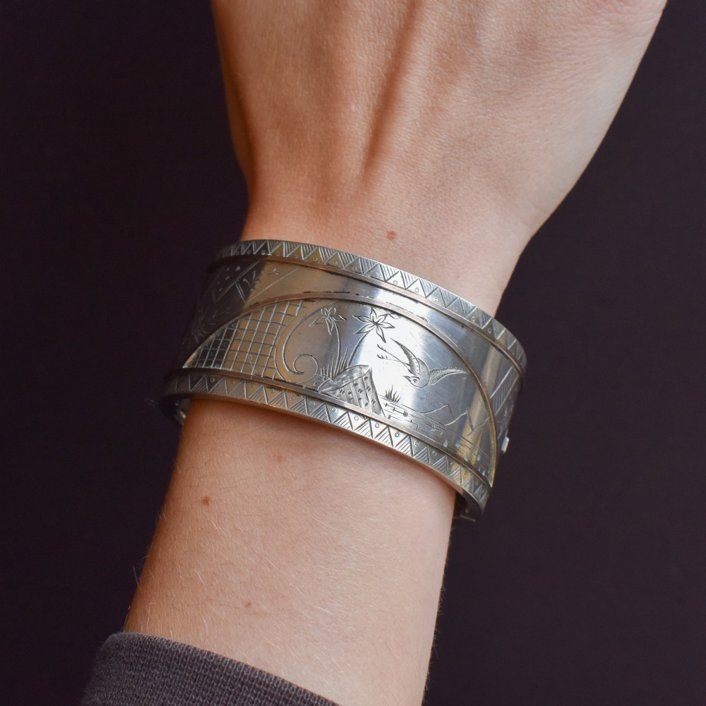 A wide antique silver cuff bangle featuring detailed hand-engraved scenes of a bird in flight, foliage, and geometric borders. View VIII