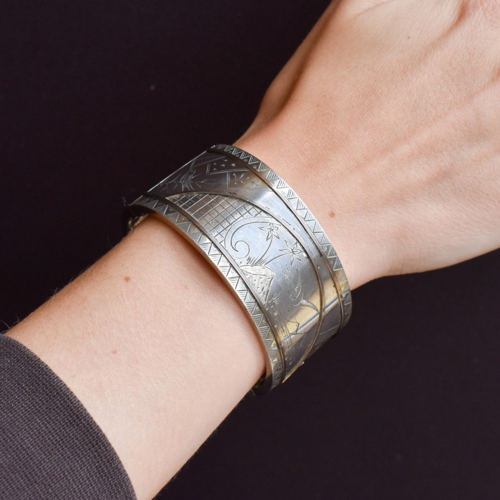 A wide antique silver cuff bangle featuring detailed hand-engraved scenes of a bird in flight, foliage, and geometric borders. View IX