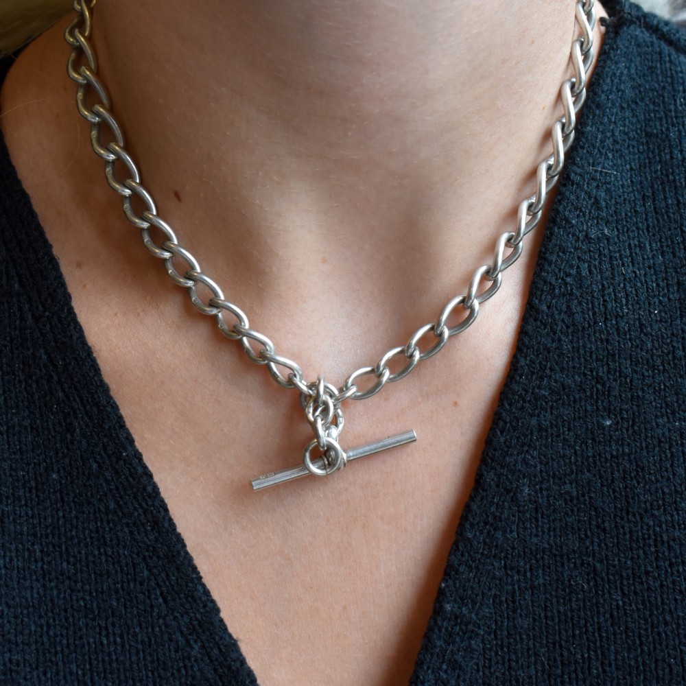An Edwardian sterling silver Albert watch chain featuring heavy oval links, a central T-bar, and a dog clip clasp. View X