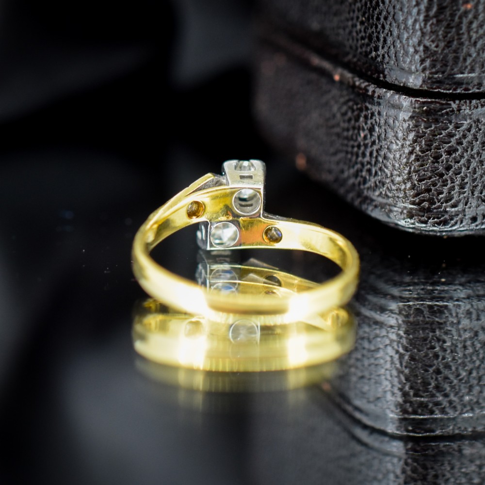 An Art Deco eighteen-carat gold and platinum twist ring featuring two round cut diamonds in a bypass setting with millegrain detailed shoulders. View IV