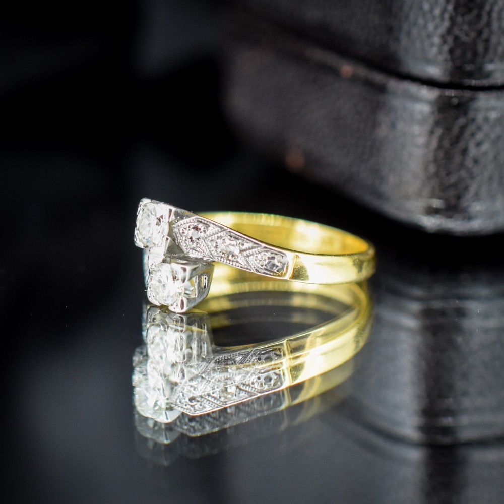 An Art Deco eighteen-carat gold and platinum twist ring featuring two round cut diamonds in a bypass setting with millegrain detailed shoulders. View V