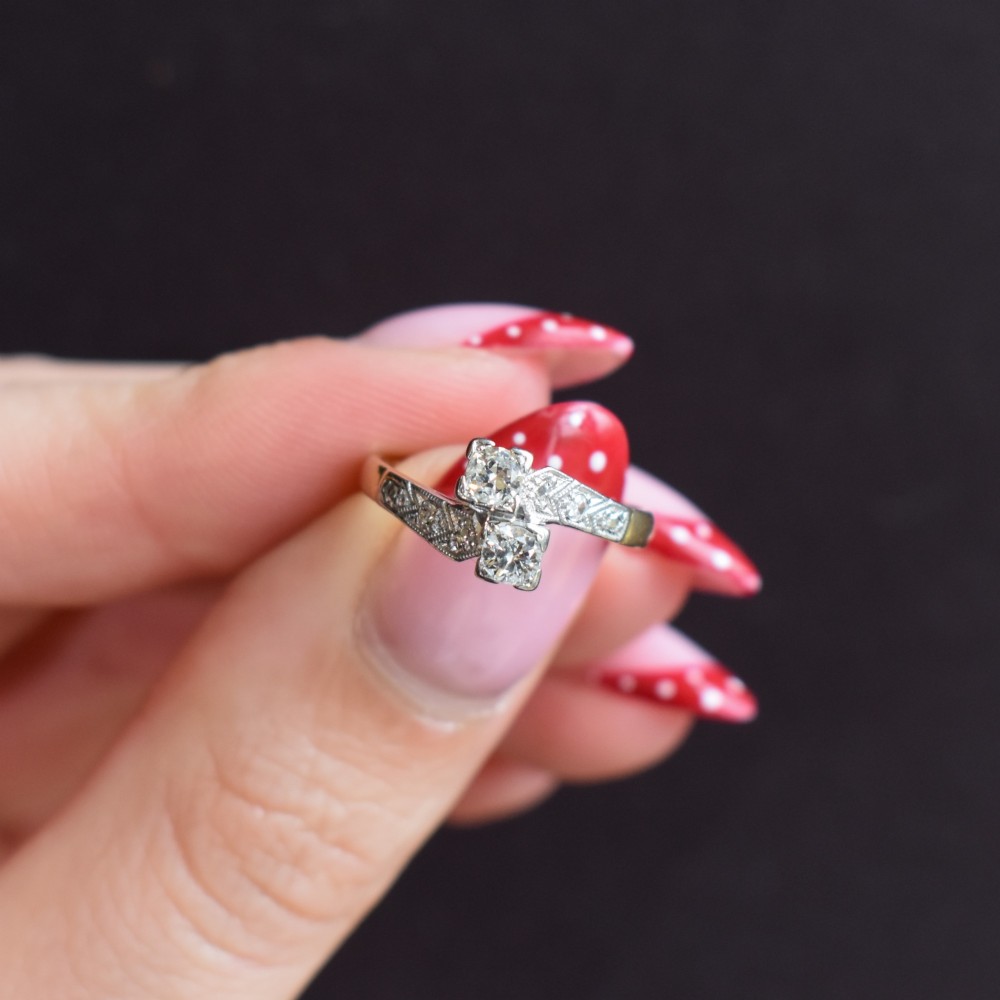 An Art Deco eighteen-carat gold and platinum twist ring featuring two round cut diamonds in a bypass setting with millegrain detailed shoulders. View VII