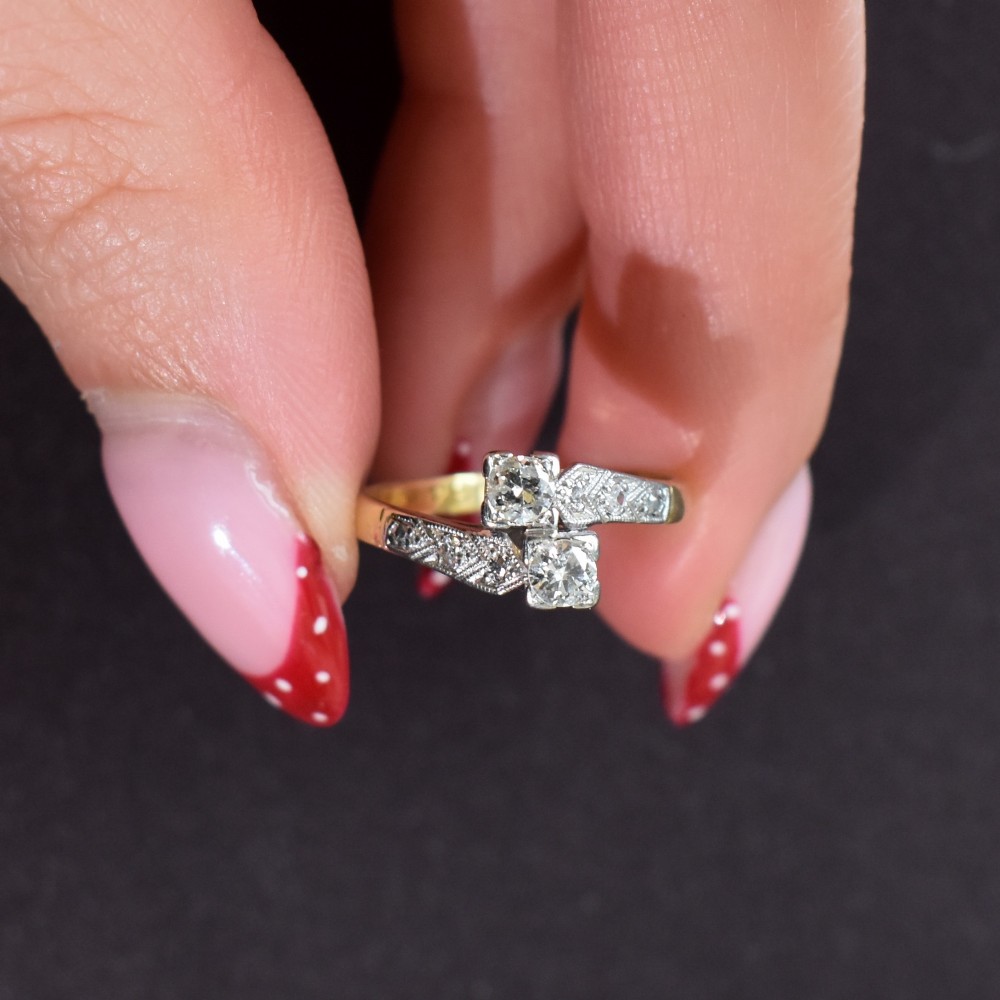 An Art Deco eighteen-carat gold and platinum twist ring featuring two round cut diamonds in a bypass setting with millegrain detailed shoulders. View VIII