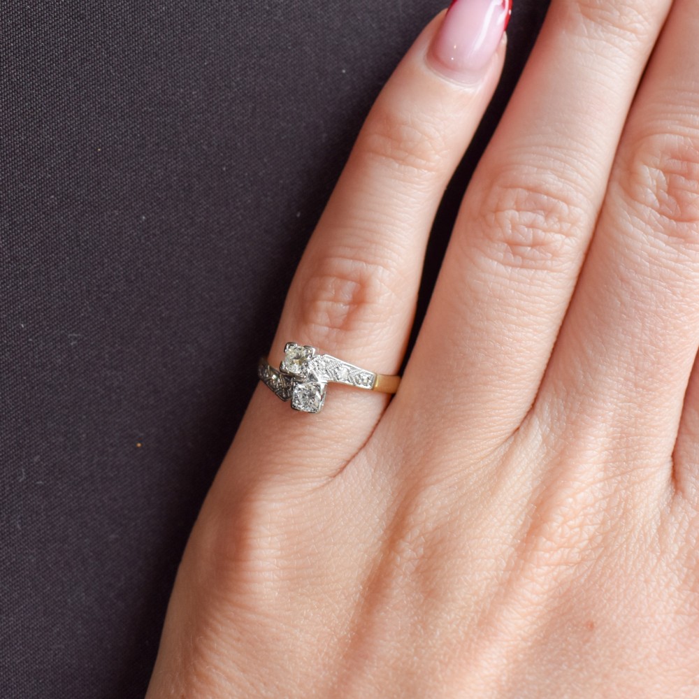 An Art Deco eighteen-carat gold and platinum twist ring featuring two round cut diamonds in a bypass setting with millegrain detailed shoulders. View IX