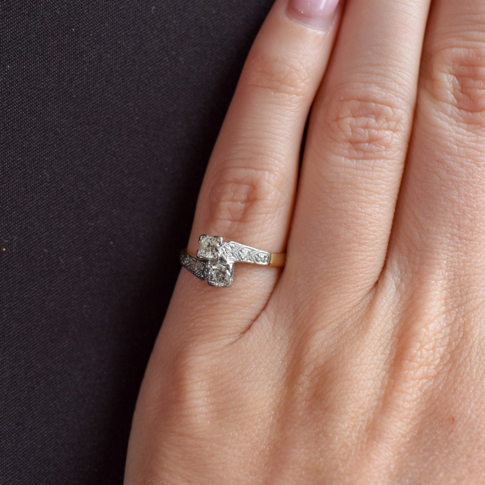 An Art Deco eighteen-carat gold and platinum twist ring featuring two round cut diamonds in a bypass setting with millegrain detailed shoulders. View X