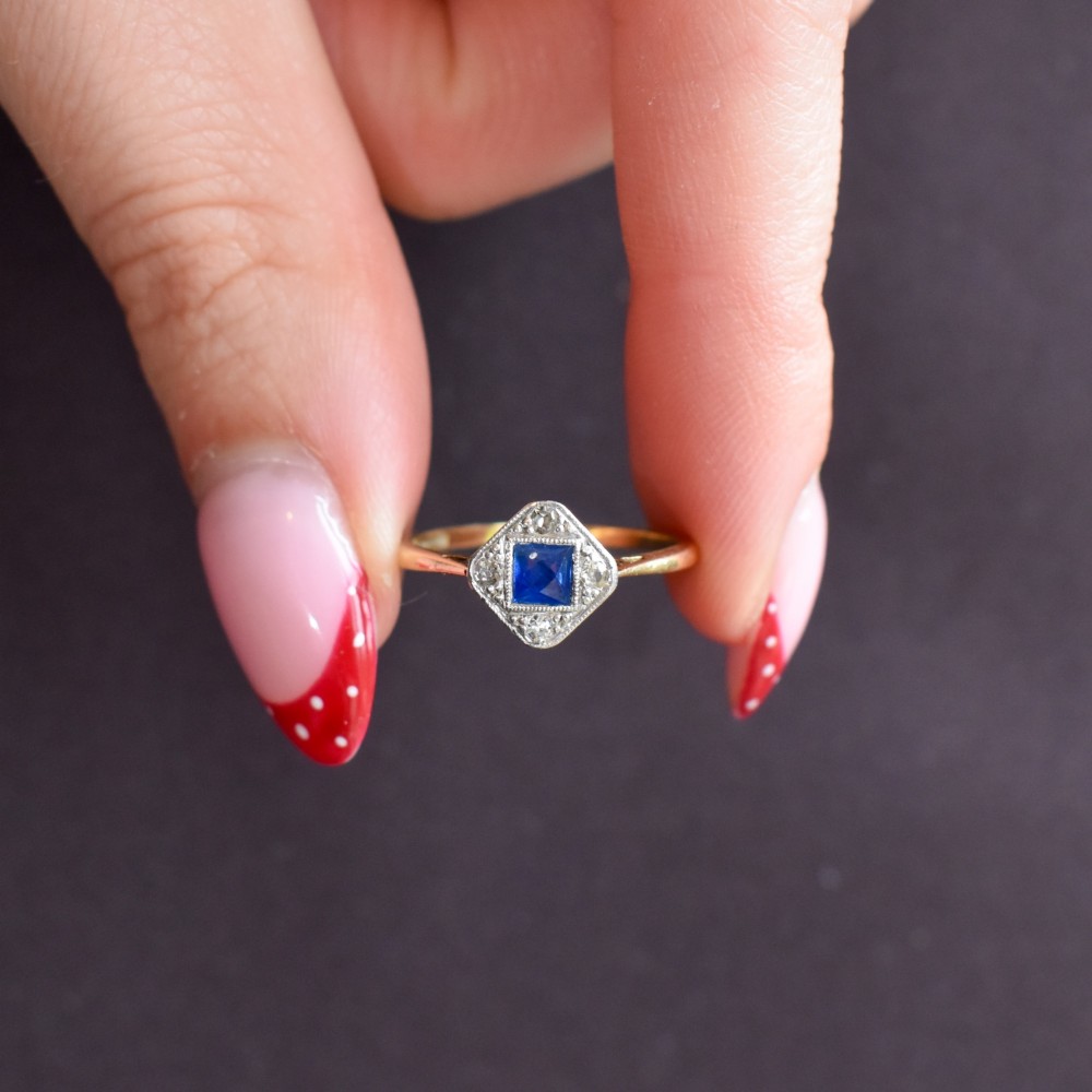 An Art Deco ring displaying a square blue sapphire surrounded by diamonds in a diamond-shaped geometric setting on an 18ct yellow gold band. View VIII
