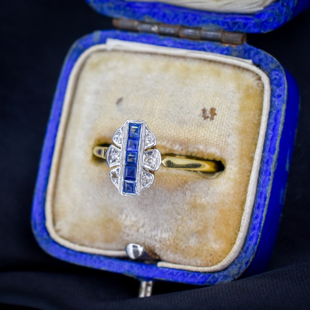 An Art Deco 18ct gold ring featuring a central vertical row of square blue sapphires flanked by diamond accents in a navette setting. View II