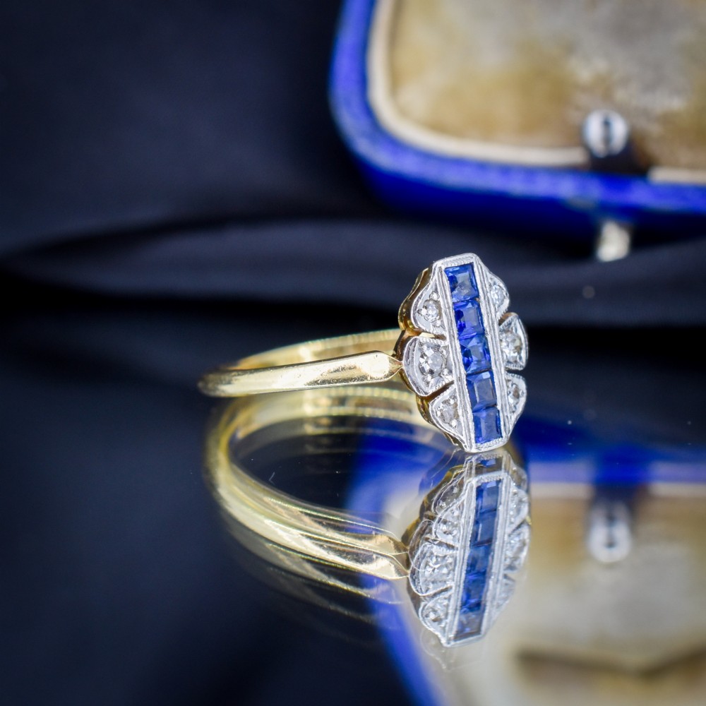 An Art Deco 18ct gold ring featuring a central vertical row of square blue sapphires flanked by diamond accents in a navette setting. View IV
