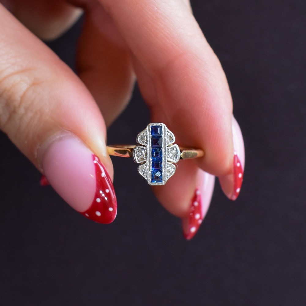 An Art Deco 18ct gold ring featuring a central vertical row of square blue sapphires flanked by diamond accents in a navette setting. View VIII