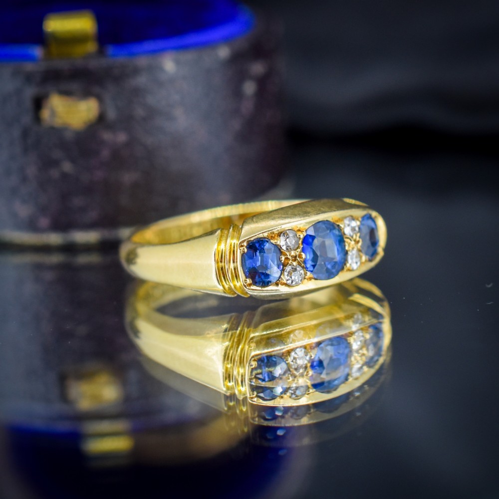 An Edwardian 18ct yellow gold boat ring set with three blue sapphires and accent diamonds in a carved setting. View V