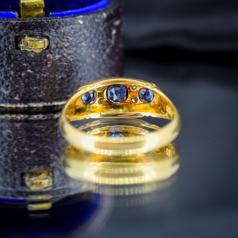An Edwardian 18ct yellow gold boat ring set with three blue sapphires and accent diamonds in a carved setting. View VI