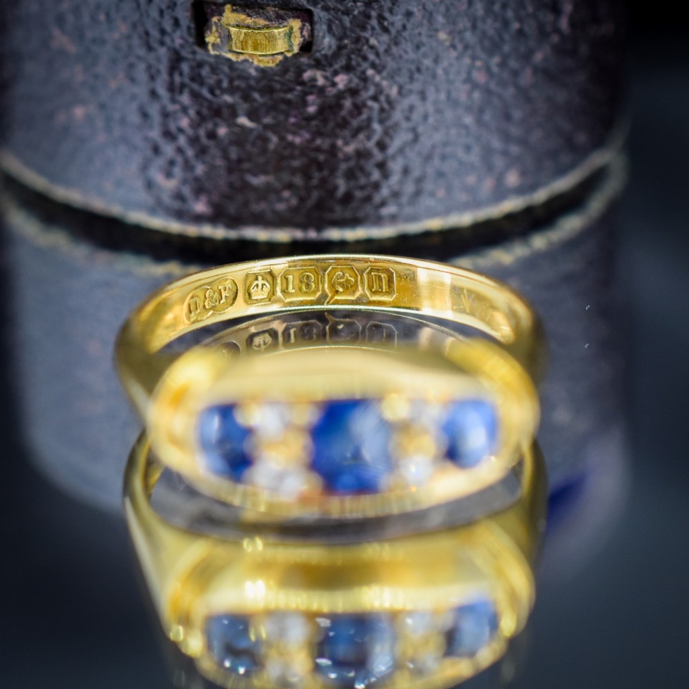 An Edwardian 18ct yellow gold boat ring set with three blue sapphires and accent diamonds in a carved setting. View VIII