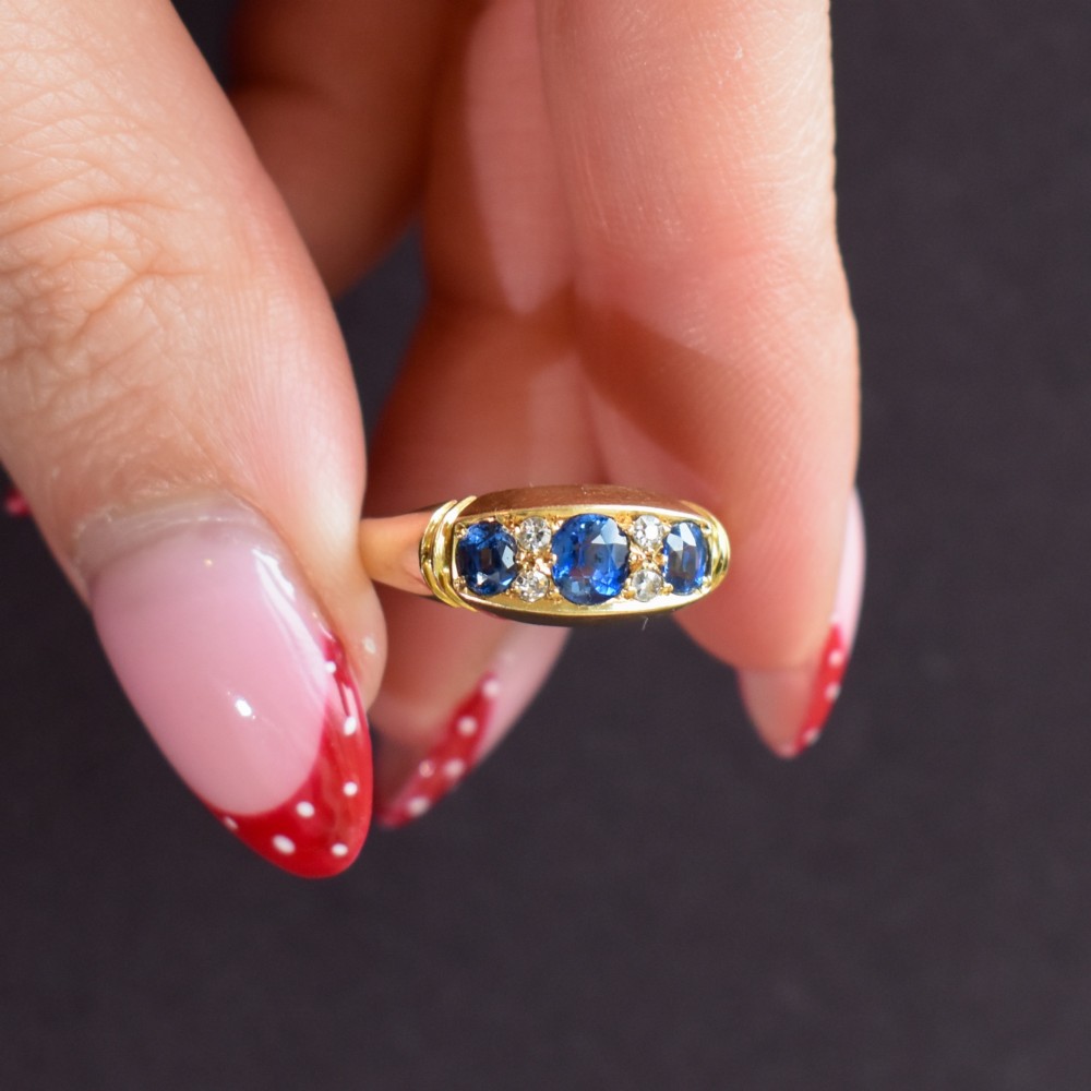 An Edwardian 18ct yellow gold boat ring set with three blue sapphires and accent diamonds in a carved setting. View IX